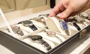 Una mano elige un reloj de una caja. Los relojes de pulsera, algunos de niquel que no se oxida, están ordenados en compartimentos.