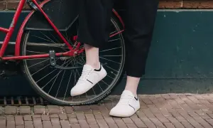 Voeten in witte barefoot schoenen naast een rode fiets. Nadelen barefoot schoenen: minder bescherming op oneffen ondergrond.