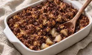 Un délicieux crumble poire chocolat, avec des morceaux de poires fondantes sous une croûte croustillante au cacao. Une cuillère en bois est plantée dans ce dessert gourmand.