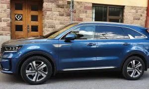 Blå laddhybrid diesel Kia Sorento parkerad framför en tegelbyggnad med en trädörr med ett hjärta.