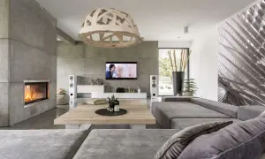 Nowoczesny salon z kominkiem i ścianą z betonu architektonicznego. Szara kanapa, drewniany stolik i designerska lampa tworzą przytulną atmosferę.