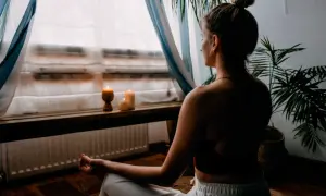 Mujer meditando en un espacio para meditar en casa, con velas encendidas y plantas.