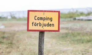 Gul skylt med texten "Camping förbjuden" på en trästolpe. Ingen husbil parkering här.