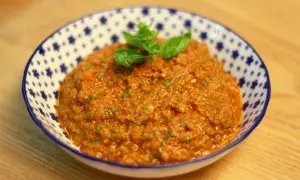 Un cuenco de pesto rosso casero, con hojas de albahaca fresca encima, listo para acompañar pasta o bruschetta.