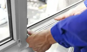 Ręce w niebieskiej kurtce montują uszczelkę w oknie, pokazując, jak uszczelnić okna na zimę.