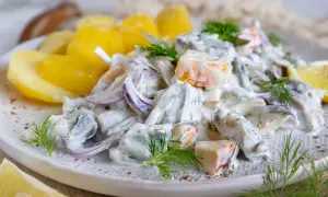 Matjessalat Hausfrauenart mit Pellkartoffeln, Zwiebeln und Dill in cremiger Sauce, garniert mit Zitronenspalten.