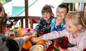 Radosna majówka w górach z dziećmi. Uśmiechnięte maluchy przy stole pełnym owoców, kefirów i słodkości.