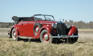 Röd cabriolet, en av de äldre tyska bilarna, parkerad på en äng med skog i bakgrunden.