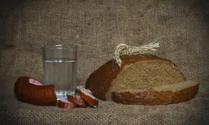 Szklanka wódki z ziemniaka, kromka chleba i kiełbasa na płóciennym tle. Proste, polskie smaki.