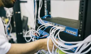 Technik podłącza kable do switcha sieciowego. Każde urządzenie ma swój unikalny adres MAC, który identyfikuje je w sieci.
