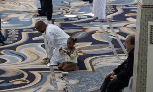 Bambina e uomini in preghiera su un tappeto decorato, un momento di pace durante il Ramadan a Roma.