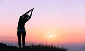 Silueta de una persona en postura de yoga al amanecer, sintiendo la energía vital del nuevo día.