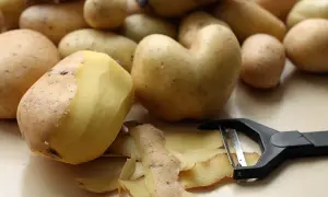 Obieraczka do ziemniaczków leży obok świeżo obranych ziemniaków. Skórki tworzą na blacie małą górkę.