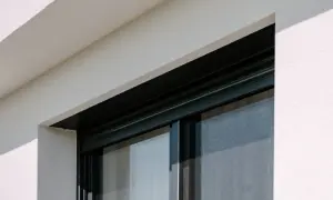 Czarne, wąskie okno łazienkowe z siatką przeciw owadom, osadzone w białej, tynkowanej ścianie.