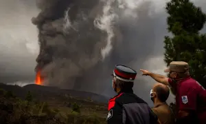 Trzej mężczyźni w maskach obserwują potężną erupcję wulkanu na La Palmie, z której wydobywa się lawa i dym. Obraz przypomina o zagrożeniu tsunami.