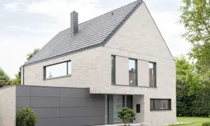 Modernes Haus mit hellem Klinker, das nicht gestrichen ist. Graues Dach, Garage und Fensterrahmen.