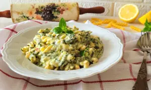 Makaron fusilli w kremowym sosie ze szpinakiem i serem, udekorowany bazylią.