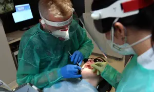 Stomatolodzy w pełnym rynsztunku ochronnym pracują przy pacjencie. To ważny element rejestru zawodów medycznych.