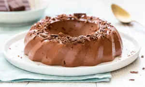 Budino al cioccolato lucido e invitante, guarnito con riccioli di cioccolato fondente, su un piatto bianco.