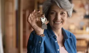Une femme souriante de plus de 65 ans tient des clés avec un pendentif maison. Elle bénéficie de la **loi alur locataire plus de 65 ans**.