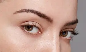 Gros plan sur des yeux marron avec des cils longs. Le sourcil gauche est légèrement plus fin, montrant comment dessiner ses sourcils pour un look naturel.