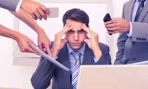 Stressad man med händer på tinningarna, omgiven av kollegor som ger instruktioner. Dålig kognitiv ergonomi leder till överbelastning.