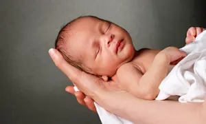 Śpiące niemowlę w ramionach, jego ciemiączko przednie kiedy zarasta, otulone białym materiałem.