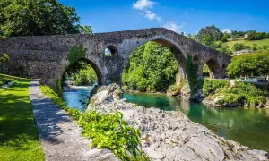 El histórico puente de Cangas de Onís cruza un río de aguas cristalinas rodeado de exuberante vegetación.