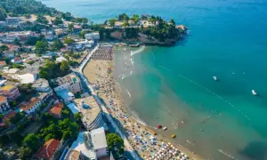 Widok z lotu ptaka na tętniące życiem czarnogórskie miasta turystyczne z plażą pełną parasoli i turystów, oraz turkusowym morzem.