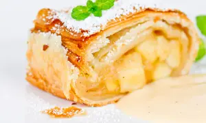 Ein Stück Apfelstrudel mit Puderzucker und Minze, serviert mit Vanillesauce.
