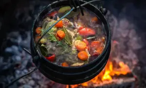 Aromatyczne dania z kociołka żeliwnego nad ogniem: mięso, marchewka, pomidory i zioła gotujące się w bulionie.