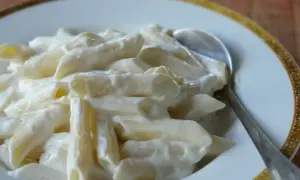 Penne z kremowym twarogiem na słodko, podane na talerzu z łyżką. Pyszne danie, które z pewnością zadowoli każdego.