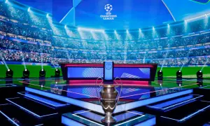 Trofeum Ligi Mistrzów na scenie z widownią w tle. Tuż obok ekran z napisem "Liga Mistrzów", który może wyświetlać tabelę wyników.