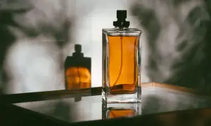 Szklany flakon perfum z bursztynowym płynem i czarną nakrętką, odbijający się w lustrzanej powierzchni.