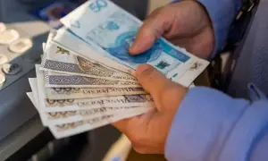 Ręce trzymają polskie banknoty. Czy to dodatek do emerytury za urodzenie 2 dzieci?