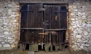 Stare, drewniane wrota do stodoły w Żarkach, zniszczone przez czas, stoją w kamienno-ceglanej ścianie.
