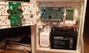 Wnętrze centrali alarmowej Satel z modułem ETHM-1 Plus, płytą główną Integra i akumulatorem.