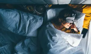 Ein Mädchen mit Hasen-Schlafmaske liegt im Bett und scheint schnell einschlafen zu wollen.