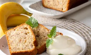 Slices of banana bread with cream and mint leaves, next to whole bananas.
