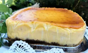 Puszysty sernik z mlekiem w proszku, z lekko przypieczoną skórką, na tle zieleni i białej koronki.