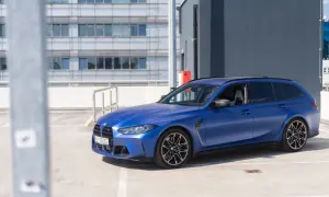 Niebieskie BMW M3 Touring na parkingu. Sportowy kombi z matowym lakierem prezentuje się dynamicznie na tle nowoczesnego budynku.