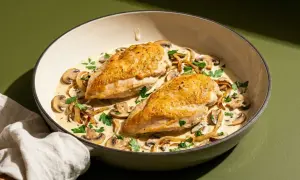 Zwei goldbraune Hähnchenbrustfilets, ein **supreme de poulet**, ruhen in cremiger Pilzsoße mit frischer Petersilie.