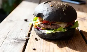 Burger maison avec pain noir, garni de salade, oignons rouges, cornichons, fromage et sauce.