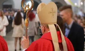 Biskup w czerwonej szacie i mitrze z krzyżem, trzyma pastorał ze złotym barankiem.