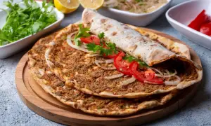 Pyszny lahmacun przepis na cienkim cieście z mięsem mielonym, pomidorami i cebulą. Obok świeża natka, cytryny i pikantne papryczki.