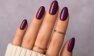 Main d'une femme aux ongles vernis d'un prune profond, une parfaite idée ongle janvier. Deux fines bagues dorées ornent les doigts.