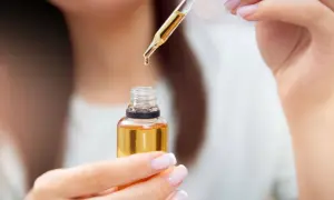 Kropla olejku rycynowego na rzęsy spada z pipetki do małej buteleczki.