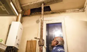 Un homme regarde un plafond délabré soutenu par une poutre rouillée. Ce **logement insalubre** montre des signes de dégradation avancée.