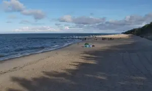 Piękny zachód słońca w Pobierowie. Ludzie spacerują po plaży, morze faluje, a niebo zdobią chmury.
