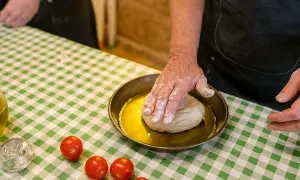 Ręce w mące wyrabiają ciasto na oliwie. Na zielono-białej kratce leżą pomidorki. Pyszne bari jedzenie w przygotowaniu.